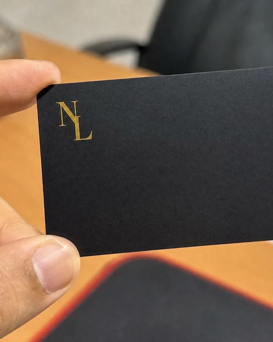 A black PVC contact card with a gold monogram, held between two fingers